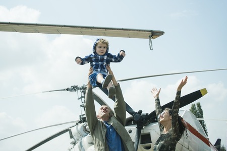 Mother, father and excited child walking in aviation museum outdoors. Happy family spend time together, on excursion, helicopter or plane on background, sunny day. Development and upbringing concept.の写真素材