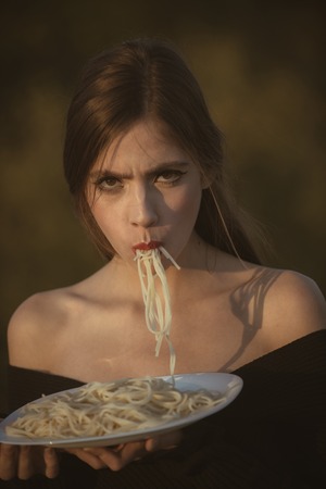 Chef woman with red lips eat pasta. Diet and healthy organic food, italy. Woman eating pasta as taster or restaurant critic. Hunger, appetite, recipe. Italian macaroni or spaghetti for dinner, cook.の写真素材