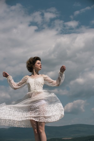 Pretty girl in white wedding dress and retro hairstyle. Beauty and fashion look in vintage style. Makeup on young face. Fashion woman model pose outdoor. Girl on sunny blue sky background in summer.の写真素材