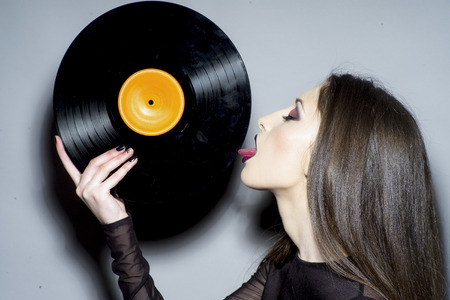 Sexy woman lick vintage vinyl disc. Woman with makeup face hold vinyl record. Fashion girl with long...