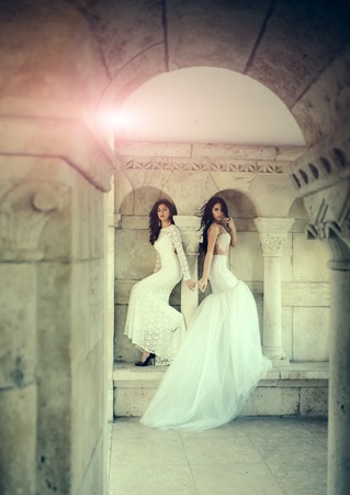 Women at stone ancient arch in summer. Sexy girls in white dress with stylish hair. Fashion model or princess in dress. Wedding fashion and beauty salon. Bride girls at wedding ceremony in castle.の写真素材