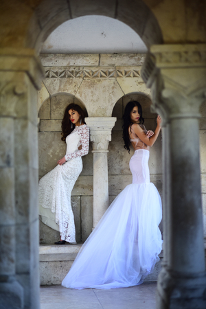 Fashion model or princess in dress. Wedding fashion and beauty salon. Bride girls at wedding ceremony in castle. Sexy girls in white dress with stylish hair. Women at stone ancient column in summerの写真素材