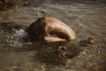 beautiful tanned woman naked relaxing and swimming in water with pineapple. Hot summer day and bright sunny light.の写真素材