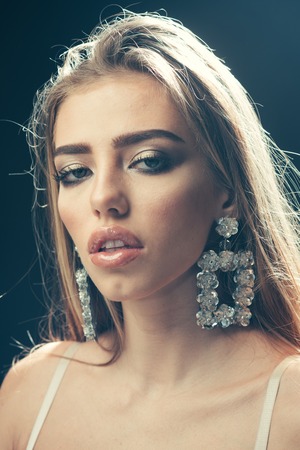 Professional makeup concept. Beauty fashion sexy girl with makeup, lipstick, eyeshadow, mascara, wears big earrings jewelry, dark studio background. Woman with sensual lips looks attractive.の写真素材