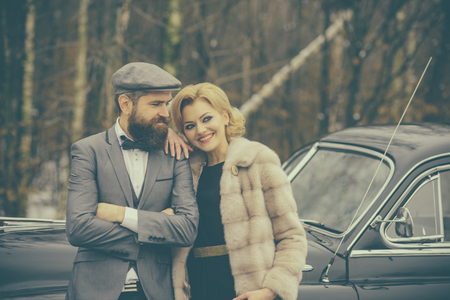 Couple in love on romantic date. Escort of girl by security. Retro collection car and auto repair by mechanic driver. Bearded man and sexy woman in fur coat. Travel and business trip or hitch hikingの写真素材