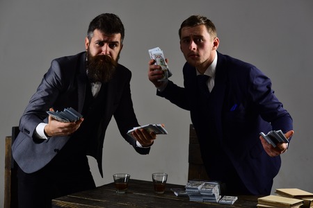 Clandestine transaction with cash. Company engaged in illegal business. Men at table with piles of money and alcohol drinks. Illegal business concept. Businessmen with packs of money looks suspicious.の写真素材