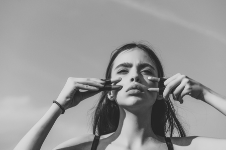 Girl posing with pink lips and lipsticks on blue sky. Woman with long brunette hair on sunny day outdoors. Fashion model with young skin on cute face. Makeup and visage conceptの写真素材