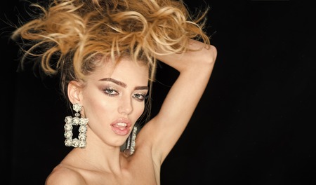 Woman with long hair and sensual lips looks attractive. Fashion and makeup concept. Fashionable sexy girl with makeup, lipstick, mascara, wears in sparkling big earrings jewelry, dark backgroundの写真素材