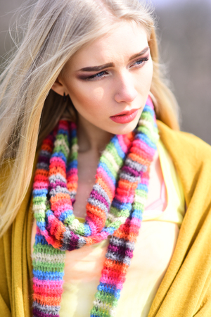 Young stylish girl with straight blond hair wearing stripped multicolored scarf, yellow jumper and cardigan posing outdoors.の写真素材