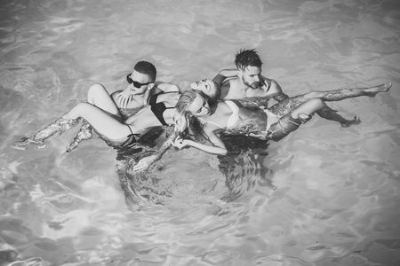 Men hold women in swimming suits in blue waterの写真素材