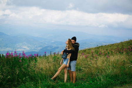 Romantic couple of pretty naked girl with bare chest and handsome bearded man in love embrace on cliff on summer day over mountain tops and skyの写真素材