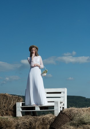 Sensual woman in wreath on long blond hair. Woman bride in wedding dress on wooden bench. Albino girl with flowers, natural beauty. Fashion model at sunny blue sky on vacation.の写真素材