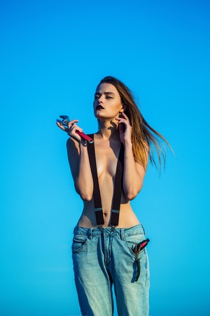 Pretty cute sexy naked woman or girl in jeans with bare chest and long hair sunny outdoor on blue sky background holding wrench or spannerの写真素材