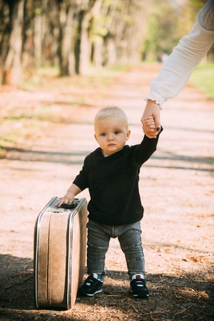 Travelling child carry suitcase on natural landscape. Travelling baby boy travel with vintage bag with mothers hand.の写真素材