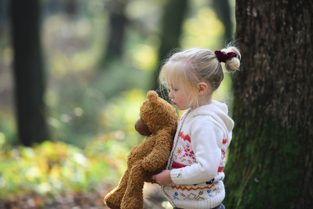 Little child walking down path with teddy bear with fall leaves and sunlight shining in background.の写真素材