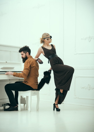 Bearded man with stylish hair playing piano while pretty girl in twenties dress and fur collar leaning on him isolated on white background.の写真素材