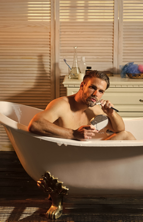 Handsome man shaving before mirror in bathroomの写真素材