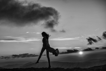 woman or girl silhouette walking at beautiful view on sunset or sunrise in blue sky with clouds and yellow orange sun in mountains on natural background.の写真素材