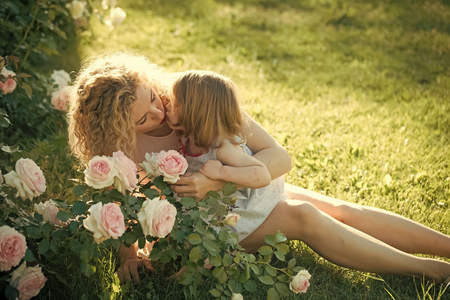 Mom kissing daughter on green grass on sunny summer dayの写真素材