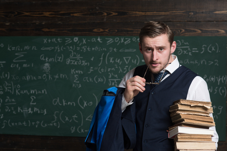 Portrait of young confident man with heap of books holding ear piece of his glasses in mouth.の写真素材