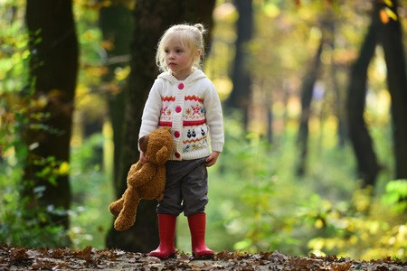 Kid with toy enjoy fresh air outdoor. Little girl in autumn forest. Child with teddy bear in fairy tale woods. Childhood, game, fun, active rest and activity.の写真素材
