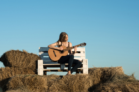Woman play guitar on wooden bench. Woman guitarist hold acoustic guitar on sunny nature.の写真素材