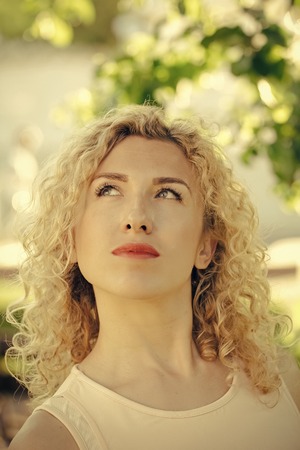 High fashion portrait of elegant woman. Girl with curly blond hair looking up on sunny r dayの写真素材