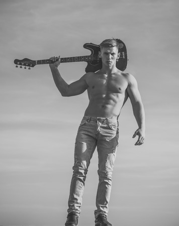 Face boy for magazine cover. Mqan face portrait in your advertisnent. Athlete guitarist with six pack, ab in jeans outdoor. Man with muscular torso hold electric guitar on blue sky. Training and playing. Sport, fitness, health concept. Music, performance, entertainment.の写真素材