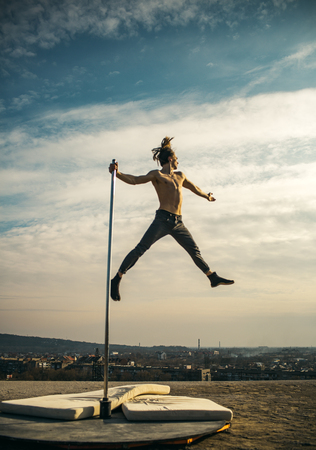 Sexy macho man fly on sky background. Pole dance sport. Strong man dancer workout on pole. Athletic guy make acrobatic elements on pylon. Young man dancing on pylon. Towards the healthier lifestyleの写真素材