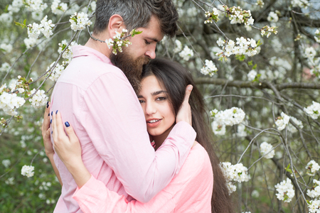 Couple in love spend time in spring garden, branches with flowers on background. Spring date concept. Couple hugs near blooming trees. Man and woman hugs in blooming garden on spring day.の写真素材
