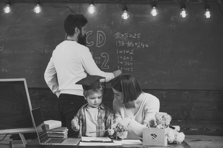 Happy kid having fun. Boy listening to mom with attention. Homeschooling concept. Family cares about education of their little smart son. Mother teaches clever son, while father writes on chalkboard on background.の写真素材