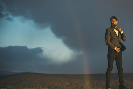 Hipster and rainbow on grey sky. Hipster in classic coat with bow tie on vacation, copy space.の写真素材