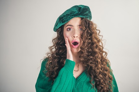 girl with curly hair at hairdresser at white wall. Fashion look and beauty concept. Fashion woman in green sweater. Retro girl with stylish makeup and hair in paris. Parisian girl in hatの写真素材