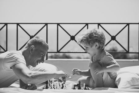 Face fashion little boy or kid in your web site. Smart toddler concept. Parent play chess with kid on terrace on sunny day. Father and little son play chess on balcony, nature and sea on background. Dad with child play intellectual gameの写真素材