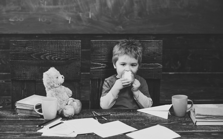 School break. Hungry kid eating apple in classroom. Small boy playing with paper planeの写真素材