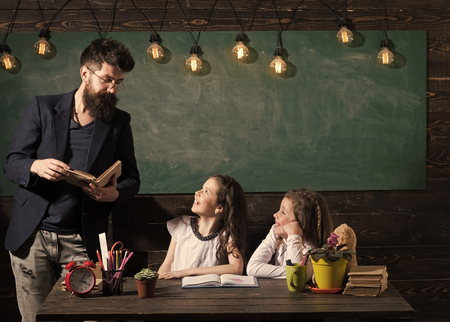 Primary school concept. Teacher and girls pupils in classroom, chalkboard on background. Curious cheerful children listening teacher with attentionの写真素材