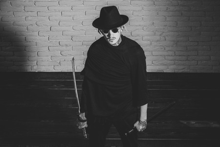 brutal tattooed man with a sword. Warrior in black sunglasses, hat and clothes, top view