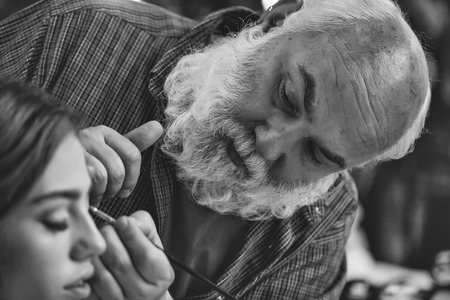 Makeup artist makes a make-up on the model. Bearded visagiste and womanの写真素材