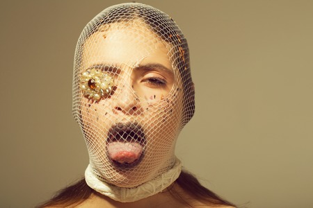 Abstract fashion portrait. Crime, criminal girl with jewelry brooch on eye showing tongueの写真素材