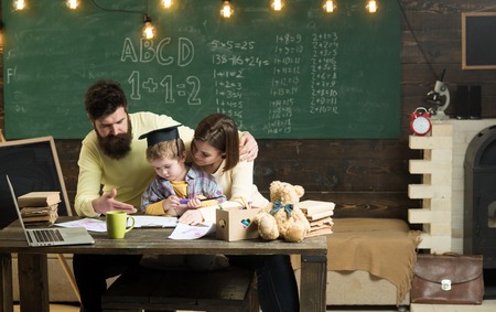 Homeschooling concept. Parents teaches son, chalkboard on background. Boy listening to mom and dad...