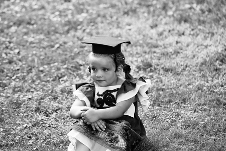 happy first-grader. Cute little girl with long hair in black graduation capの写真素材