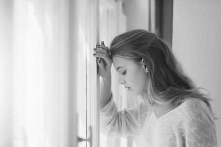 girl is sad at the window. Pretty girl standing at windowの写真素材