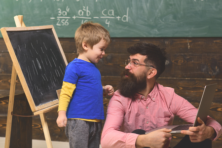Father and son in classroom. Side view man and kid looking at each other with amusement. Guy in pink shirt sitting on floor with laptopの写真素材