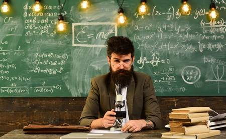 Businessman with glasses and optical instrument at desk. Bearded man work with microscope. Man with beard and mustache in school. Scientist make research on chalkboard. Science and studyの写真素材