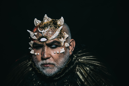 Alien, demon, sorcerer makeup. Man with third eye, thorns or warts. Demon on black background, copy space. Senior man with white beard dressed like monster in darkness. Horror and fantasy conceptの写真素材