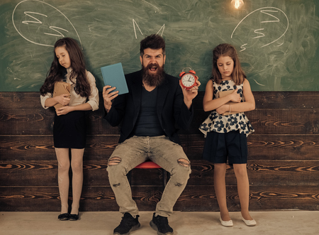 unbearable lessons. Teacher and girls pupils in classroom, chalkboard on background. Children and teacher with drawn by chalk horns. Man with beard and pretend sleeping schoolgirls. Horrible lesson concept.の写真素材
