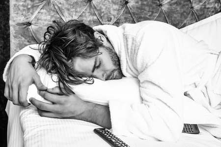 concept of fatigue. bearded man on bed with remoteの写真素材