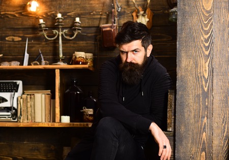 Spending great time at home. Man with beard looks strictly. Man bearded enjoy evening, wooden background. Guy in cozy warm atmosphere relaxing but looks tenseの写真素材