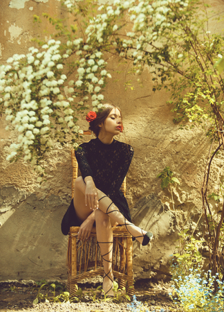 Female fashion, beauty and advertisement concept. Adorable woman sitting on wicker chair under blossoming flowersの写真素材