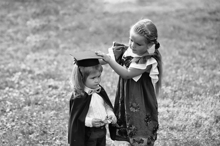 children play in the university. Cute girl dressing small boy in graduation hat and robeの写真素材